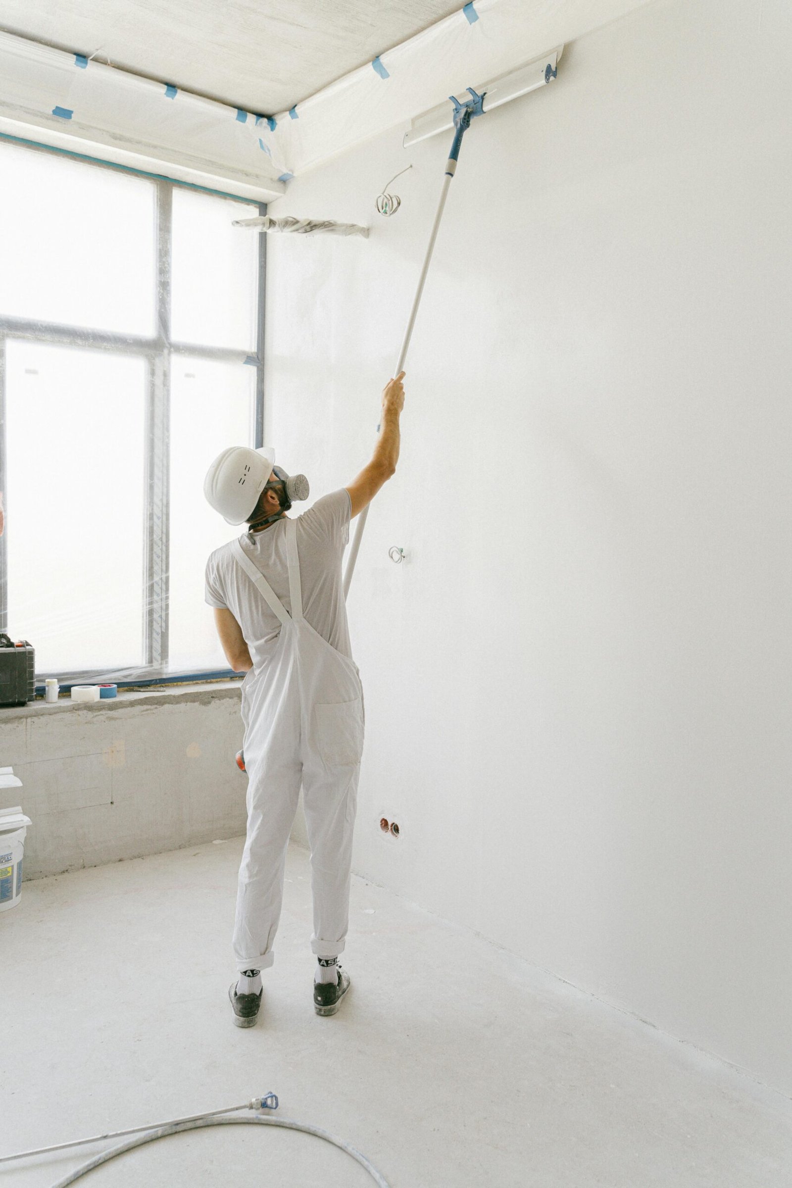 service-1 Adult painter in white uniform painting an indoor wall with a roller.